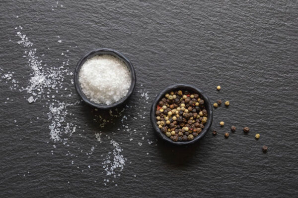 Salt and pepper. Sea salt and peppercorns in  small black dishes on black table