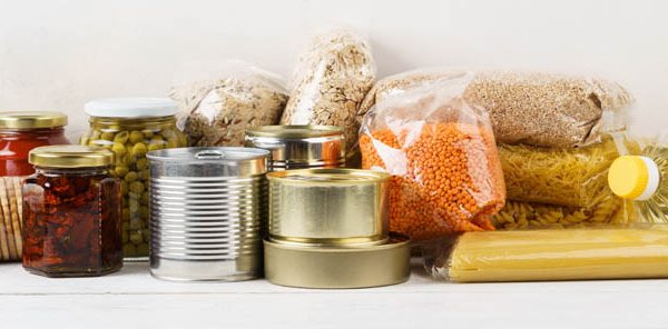 Various canned food and raw cereal grains on a table. Set of grocery goods for cooking, delivery or donation.