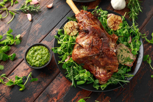 Roast Lamb leg with mint sauce, rosemary and garlic. on black plate, wooden table.